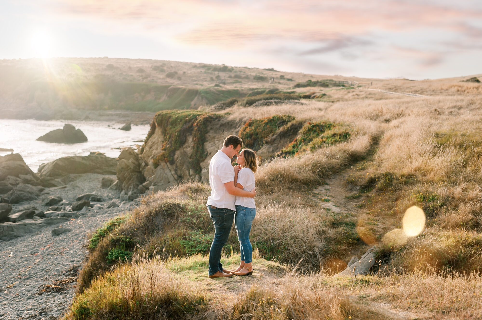 Couple standing on a small cliff of the central Coast, hold one another for their Cambria Engagement Session